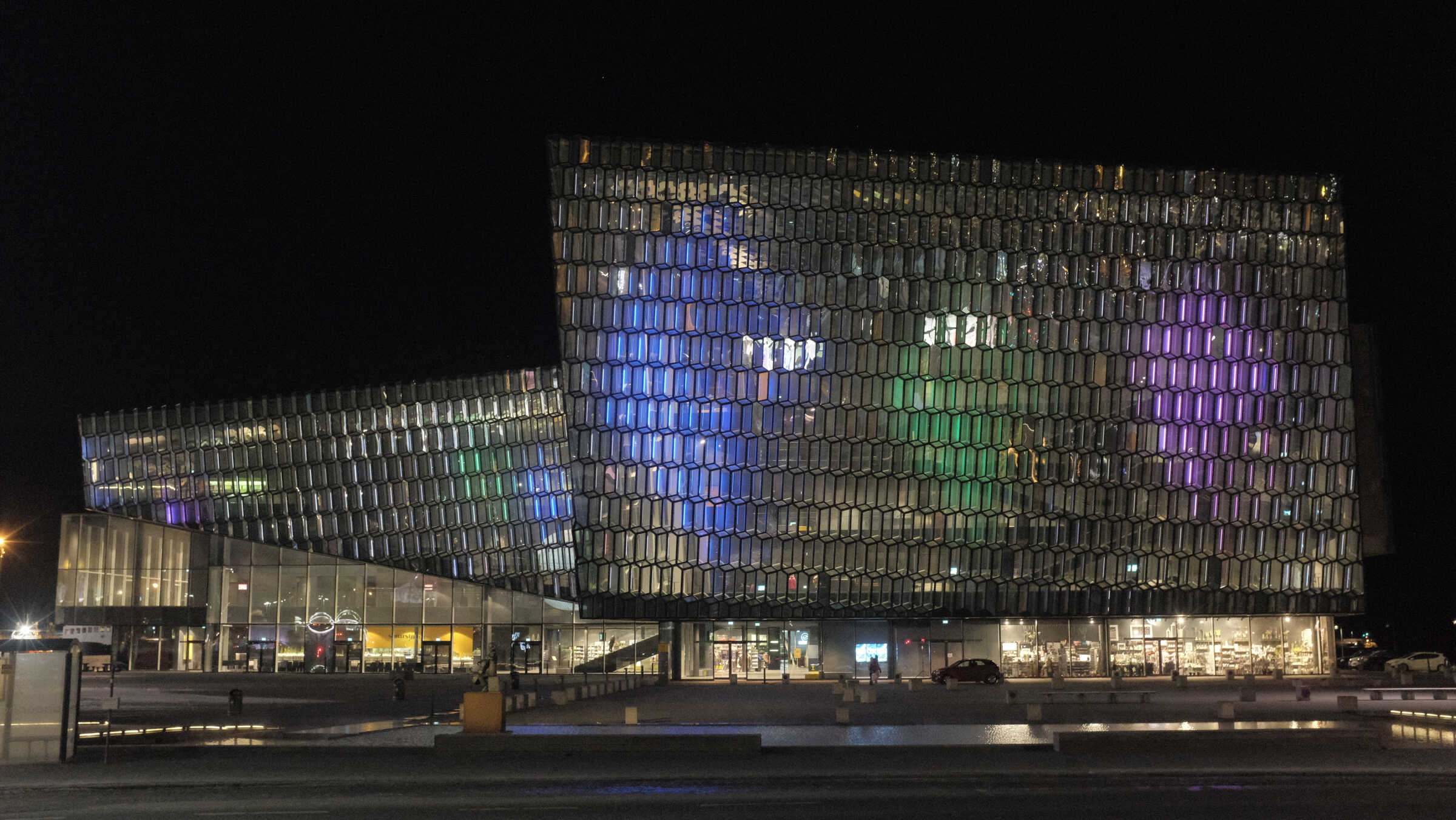 Wide nighttime view of Reykjavík's Harpa concert hall with the Dice projection illuminating its honeycomb glass façade in clusters of magenta, green, and blue