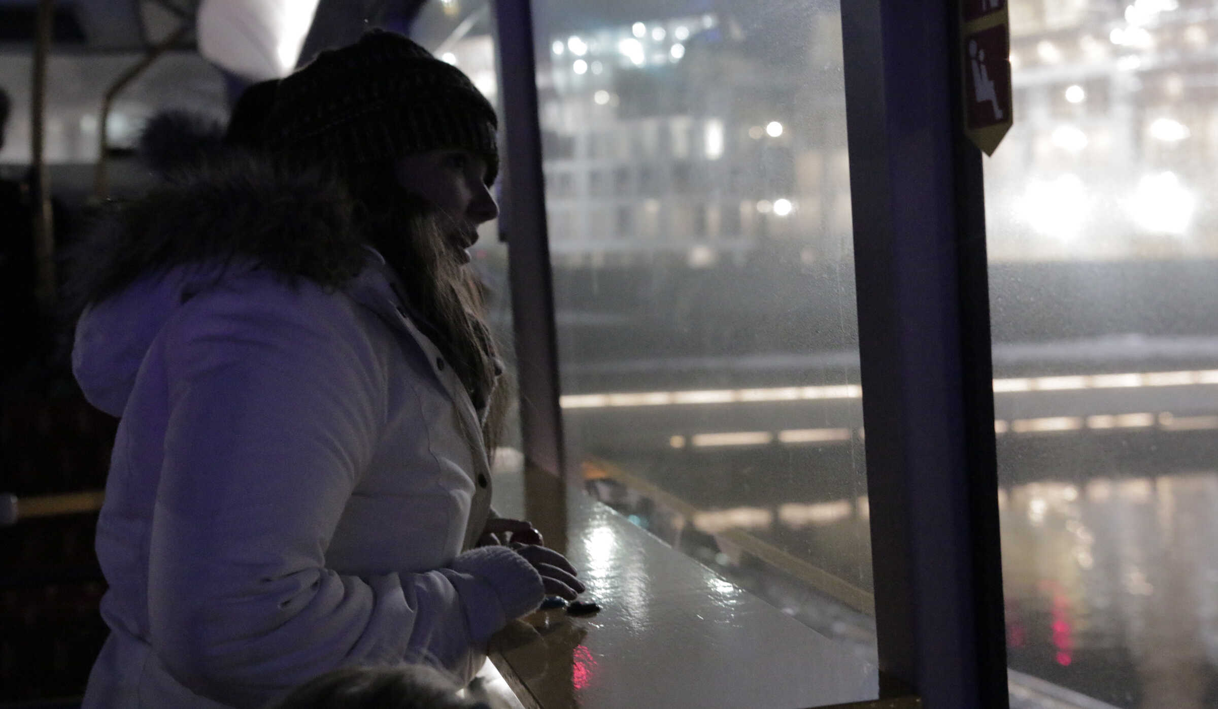 A visitor in a winter coat and beanie operating the Dice controller from inside Harpa, looking out toward the illuminated façade across the plaza