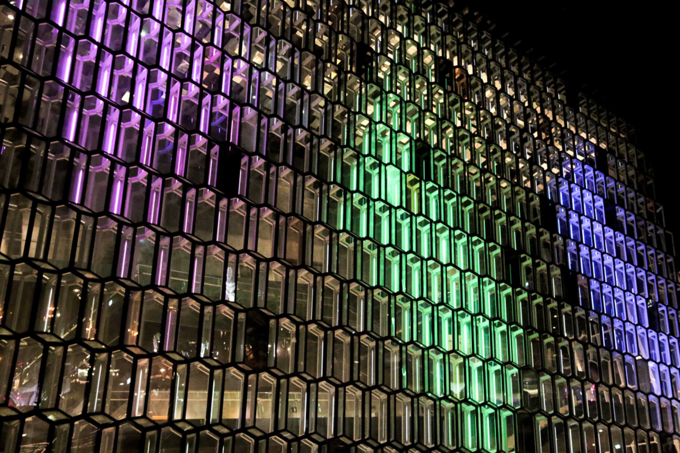Close-up of Harpa's hexagonal glass panels lit by the Dice projection, showing magenta, green, and blue light spilling across individual cells